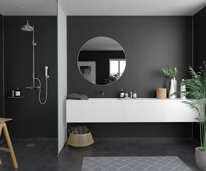 Modernt badrum med mörka väggar, rund spegel, dusch, vit förvaring, växt och trädetaljer.