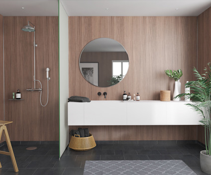 Modernt badrum med dusch, cirkulär spegel, växter och vita skåp mot en träpanelvägg.