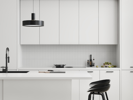 Modernt kök med vit inredning, svart hängande lampa, diskho, och två svarta barstolar vid köksön.