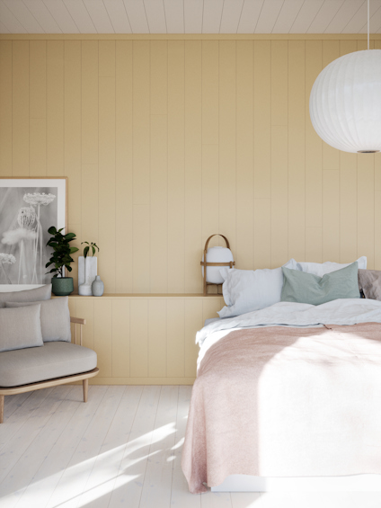 Sovrum med ljus träpanelvägg, säng med beige överkast, fåtölj, gröna växter och en rund vit taklampa.