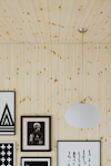 Ljusa träpaneler på vägg och tak, flera svartvita tavlor och en rund hängande lampa.