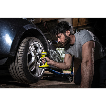 Person använder en borrmaskin för att lossa ett däck på en bil i ett garage.