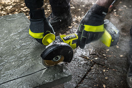 En person använder en batteridriven slipmaskin för att skära en stenplatta utomhus.