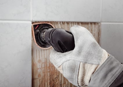 Hand i arbetshandske använder verktyg på kaklat vägg.