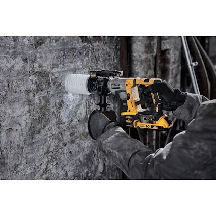 Person i arbetskläder borrar i en rå stenmur med en gulsvart Dewalt borrmaskin.