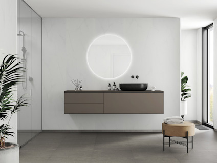 Modernt badrum med svävande handfat, rund upplyst spegel, glasdusch och stora fönster.