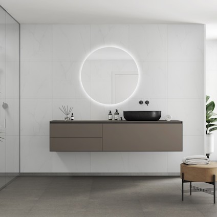 Modernt badrum med väggmonterad grå skåp, rund spegel med belysning och svart handfat. Gröna växter i hörnet.