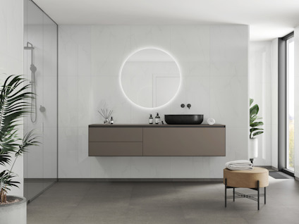 Modernt badrum med en rund, ljus spegel ovanför ett flytande skåp och svart handfat. Växt i förgrunden.