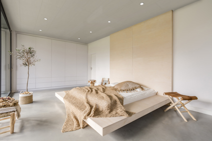 Ljust sovrum med minimalistisk inredning, ljusa träelement, grön växt och stickad pläd på sängen.