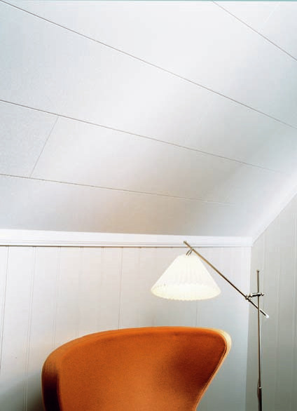 Orange stol, golvlampa med skärm i hörn av rum med ljusa väggar och tak i vita paneler.