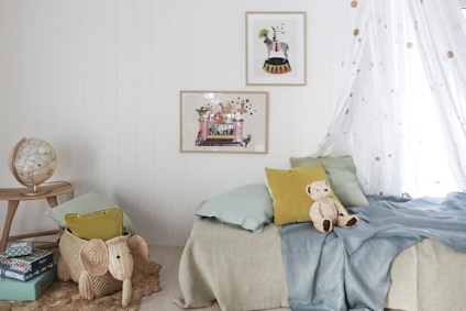 Sovrum med en säng täckt med blå och beige sängkläder, gosedjur, en jordglob, och tavlor på väggen.