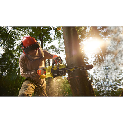 Person som sågar träd med en grön motorsåg i skogsmiljö. Solsken i bakgrunden.