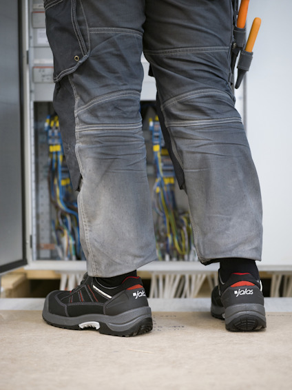 Person i arbetskläder står framför ett öppet elskåp med kablar.