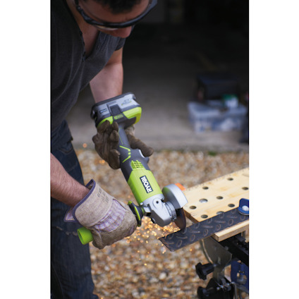 Person använder en grön batteridriven vinkelslip från Ryobi, gnistor flyger från metallplatta. Använder skyddsglasögon och handskar.