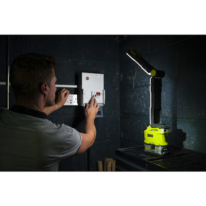 Person som arbetar vid en elcentral i ett svagt upplyst rum, med en arbetslampa som lyser upp området.