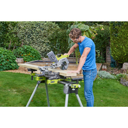 Person i blå tröja använder en kap- och geringssåg utomhus, omgiven av grönska.