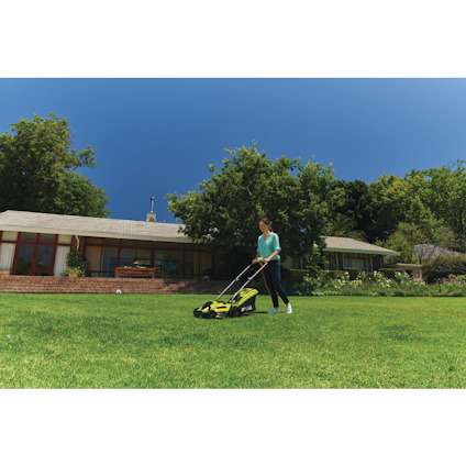 Person som klipper gräset med en grön gräsklippare på en stor gräsmatta framför ett hus.
