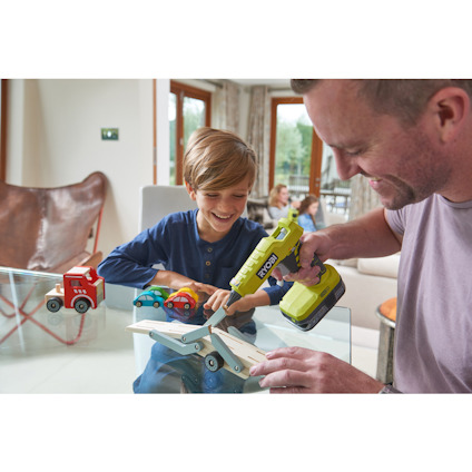 En vuxen och ett barn bygger en leksaksbil. Vuxen använder en grön Ryobi-skruvdragare.