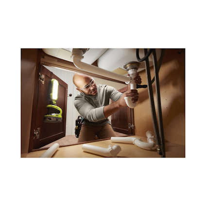 En person utför rörmokararbete under ett diskbänksskåp med verktyg vid sidan.