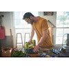 Man wearing a yellow shirt using a green nail gun on a workbench indoors.