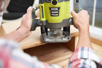 Person som använder en grön och svart Ryobi 1600W handöverfräs på träyta.