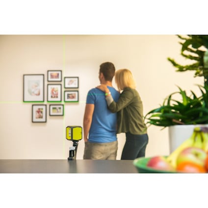 Personer står framför en vägg med inramade bilder, laserlinjer syns på väggen.