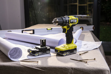 Batteridriven borrmaskin med laddare, batterier, papper och skruvar på ett bord.