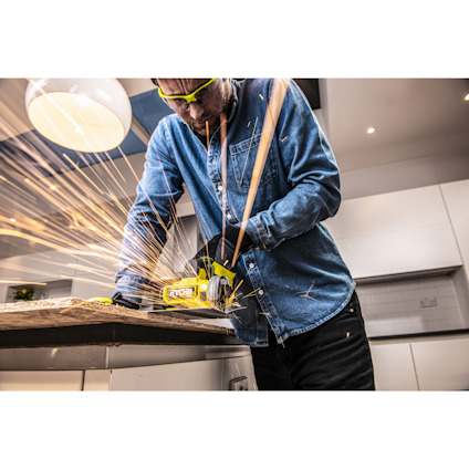 Person i jeansskjorta använder en RYOBI-slipmaskin som genererar gnistor på en träyta.