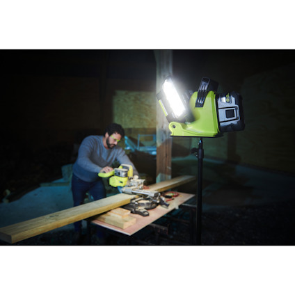 Arbetslampa lyser över en man som mäter träplankor i ett mörkt rum med verktyg på ett bord.