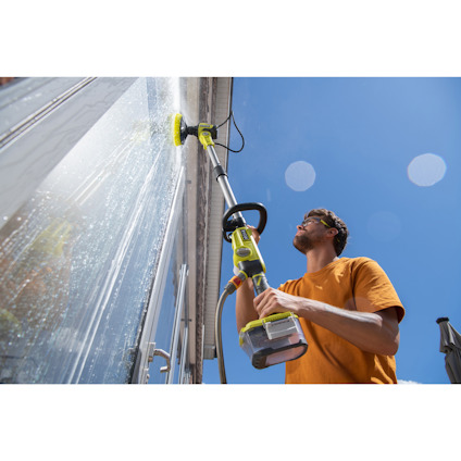 Person som tvättar fönster med en batteridriven teleskpoisk rengöringsborste av märket RYOBI under klar himmel.