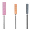 Tre cylindriska slipstift i rosa, orange och grå färg med metallhandtag på vit bakgrund.