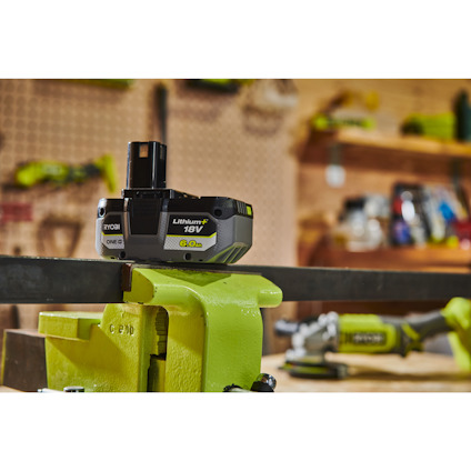 18V Ryobi Lithium+ batteri inställt i ett skruvstäd på en verkstadsbänk. Bakgrund med verktyg.
