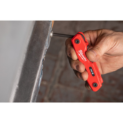 Hand håller ett rött multitool från Milwaukee, används för att skruva i en metallbit.