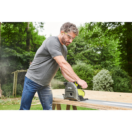 Man som använder en grön och svart cirkelsåg på en träskiva utomhus.