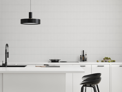 Modernt kök med vita skåp, svart kran, svarta stolar, hängande svart lampa och vit kaklad vägg.