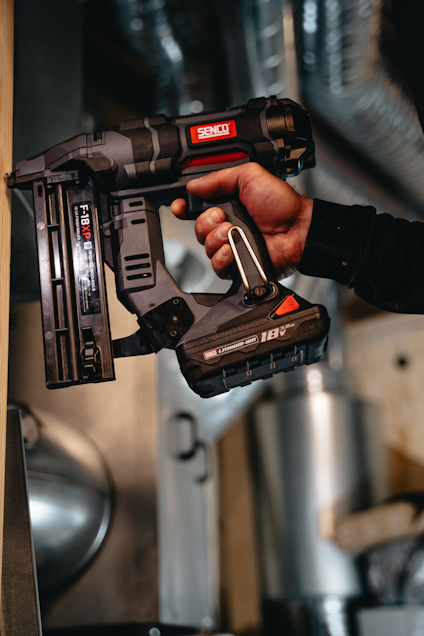 Person som håller en svart batteridriven spikpistol med märkning "Senco" och "18V".
