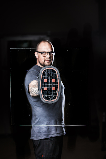 Person med glasruta och skyddsdräkt, synlig tatuering på armen.