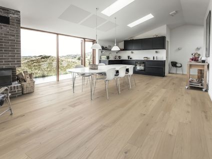 Modernt kök och matplats med träparkett, vita stolar, svart skåp, stora fönster och utsikt över naturen.