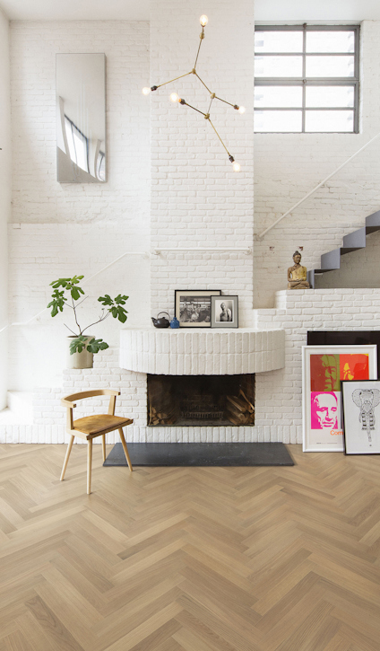 Vardagsrum med vit tegelvägg, eldstad, modern hänglampa, trästol, växt och konstverk på golvet. Herringbone parkettgolv.