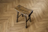 Sliten träpall med tre ben på fiskbensparkettgolv.