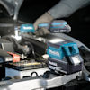 Makita batteri och verktyg vid bilmotor, handskar synliga.