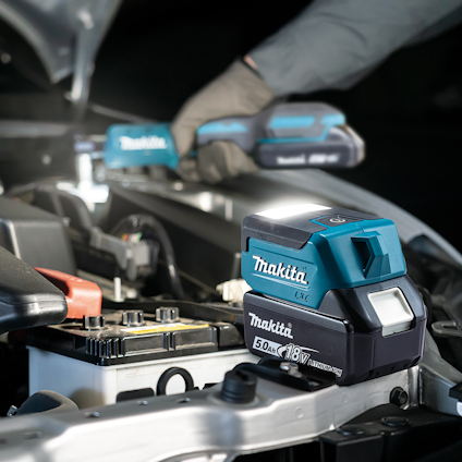 Makita batteri och verktyg vid bilmotor, handskar synliga.