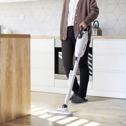 Person som använder en stående dammsugare i ett modernt kök.