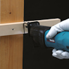 En person håller en blå Makita sticksåg och skär genom en träregel med en skruv.