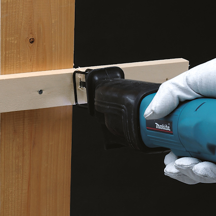 En person håller en blå Makita sticksåg och skär genom en träregel med en skruv.