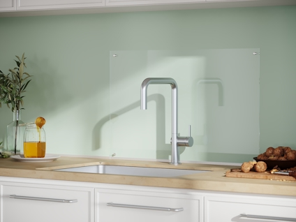 Köksbänk med diskho och kran, trägolv, glasbakgrund och bröd på bänken. Gröna skåp och dekorativa växter.