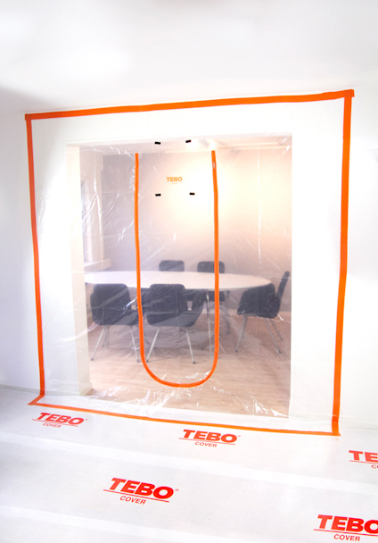 Plastdörr med orange kant och U-formad dragkedja, monterad i en dörröppning, med rum och möbler synliga bakom. Texten "TEBO" förekommer.