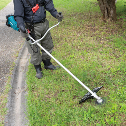 Person trimmer gräs vid en trottoarkant med en blå och svart grästrimmer.