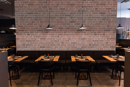Restauranginteriör med tegelvägg, fyra bord med svarta stolar och hängande lampor ovanför.