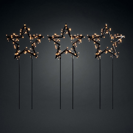 Tre svarta stjärnor på pinne med små ljus som lyser mot en mörk bakgrund.